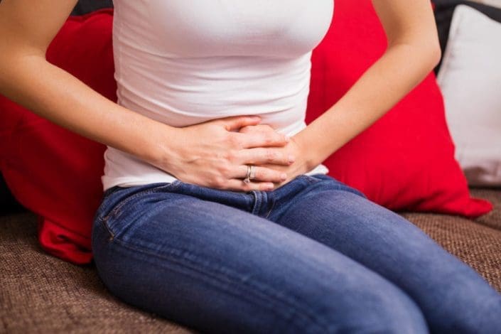 Woman suffering from menstrual cramps and holding her stomach while sitting on couch