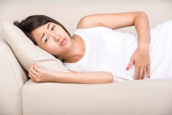 A woman suffering from stomach pain lays on a couch. Several types of diarrhea medicine are available over-the-counter to help you feel better and ease your symptoms.