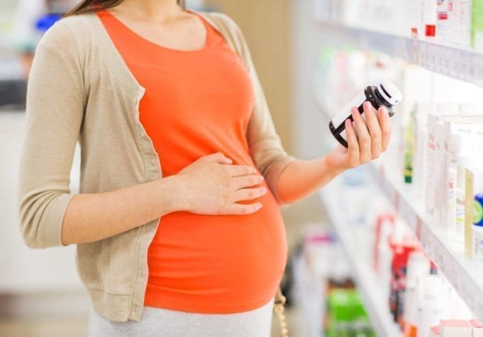close up of pregnant woman reading label on a medicine bottle at the pharmacy