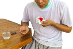 Male patient holding a bloody tissue in one hand and medicine in the other hand