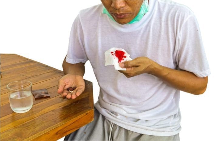 Male patient holding a bloody tissue in one hand and medicine in the other hand