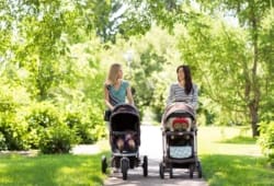 Two mothers walk their babies in strollers through the park