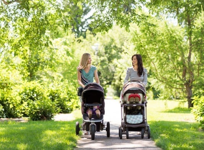 Two mothers walk their babies in strollers through the park