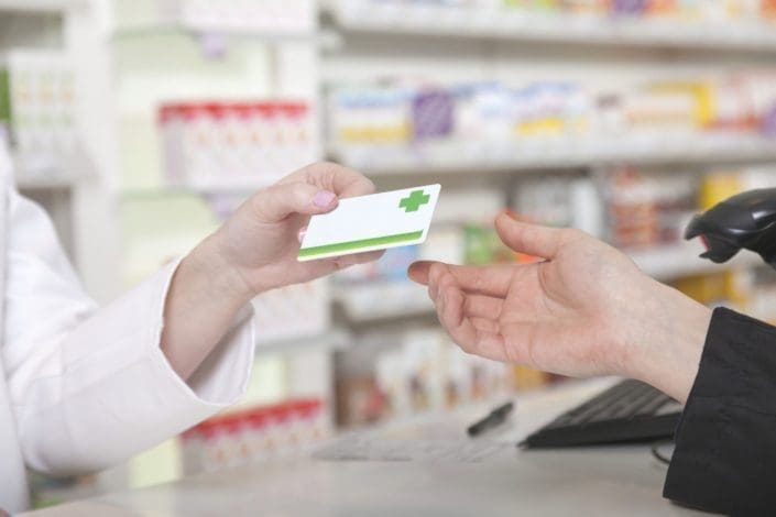 patient hands prescription medicine discount card to pharmacist
