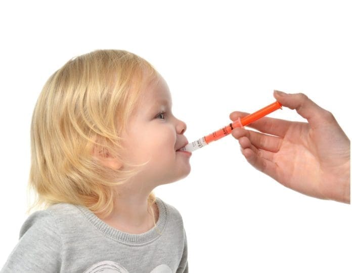 Young child takes an oral cold medicine from a syringe