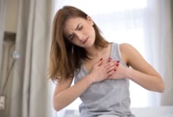 A woman having chest pains places her hands over her heart. Cardiomyopathy is a disease that causes your heart muscles to become enlarged, which can weaken your heart over time.