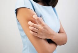 a woman with keratosis pilaris scratches the back of her arm