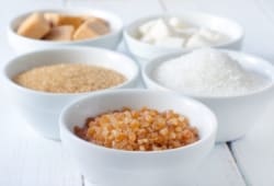 Five small white bowls, each filled with a different sugar substitute, sitting on a white table