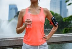A sweaty woman dressed in workout clothes standing outside in the city holding a bottle of water