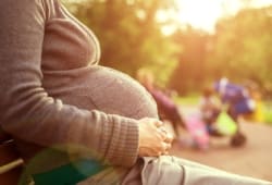 pregnant woman sitting on bench with hands on belly