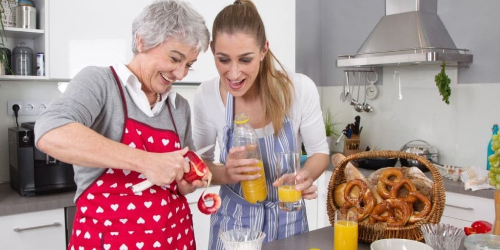 Senior mother and daughter making healthy breakfast together in kitchen.