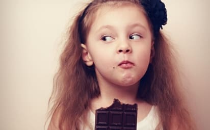 Girl eating large chocolate bar and looking to see if anyone is watching
