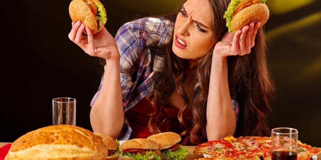 A young girl surrounded by plates of hamburgers and pizza.
