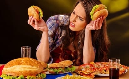 A young girl surrounded by plates of hamburgers and pizza.
