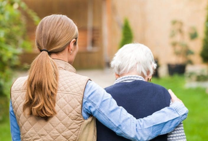 female caregiver puts her arm around an elderly woman as they walk outside