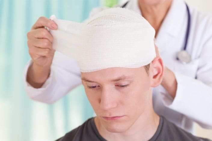 Female doctor wrapping the head of a young man with gauze