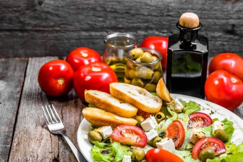 Plate of salad, tomatoes, olives, and olive oil sitting on table