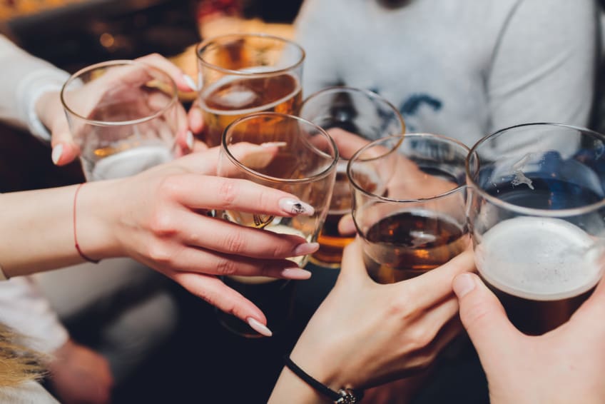 Close up shot of group of people clinking glasses with wine or champagne in front of bokeh background. older people hands.