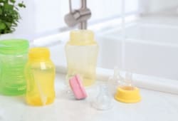 Baby bottles and nipples sit on a white countertop beside the kitchen sink after being washed.