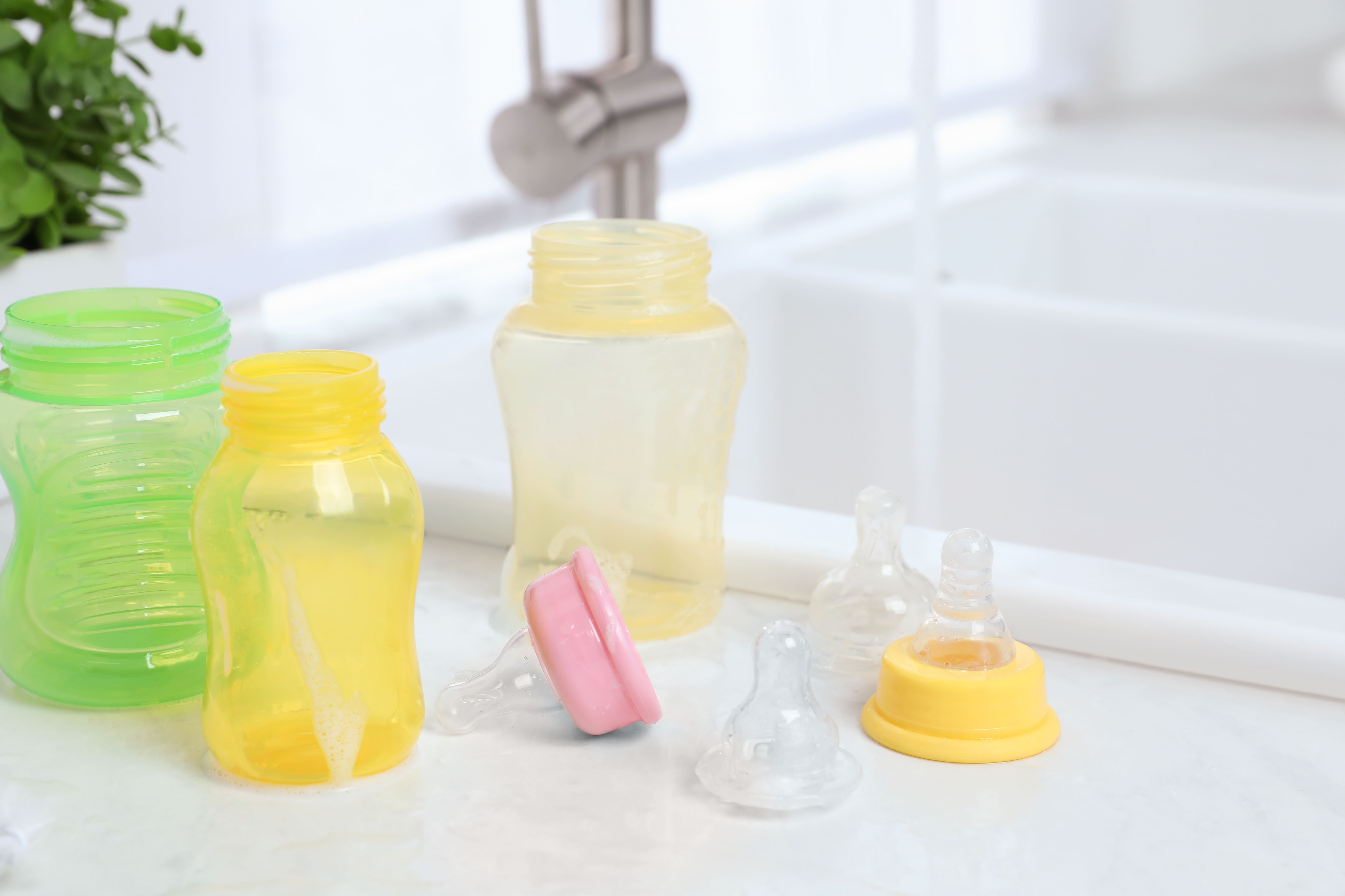 Baby bottles and nipples sit on a white countertop beside the kitchen sink after being washed.