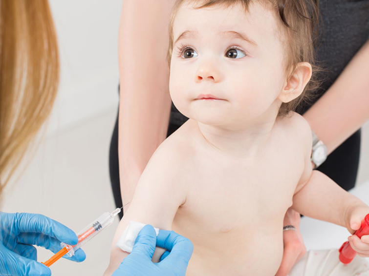 A gloved doctor is poised to give a toddler a shot in the arm.