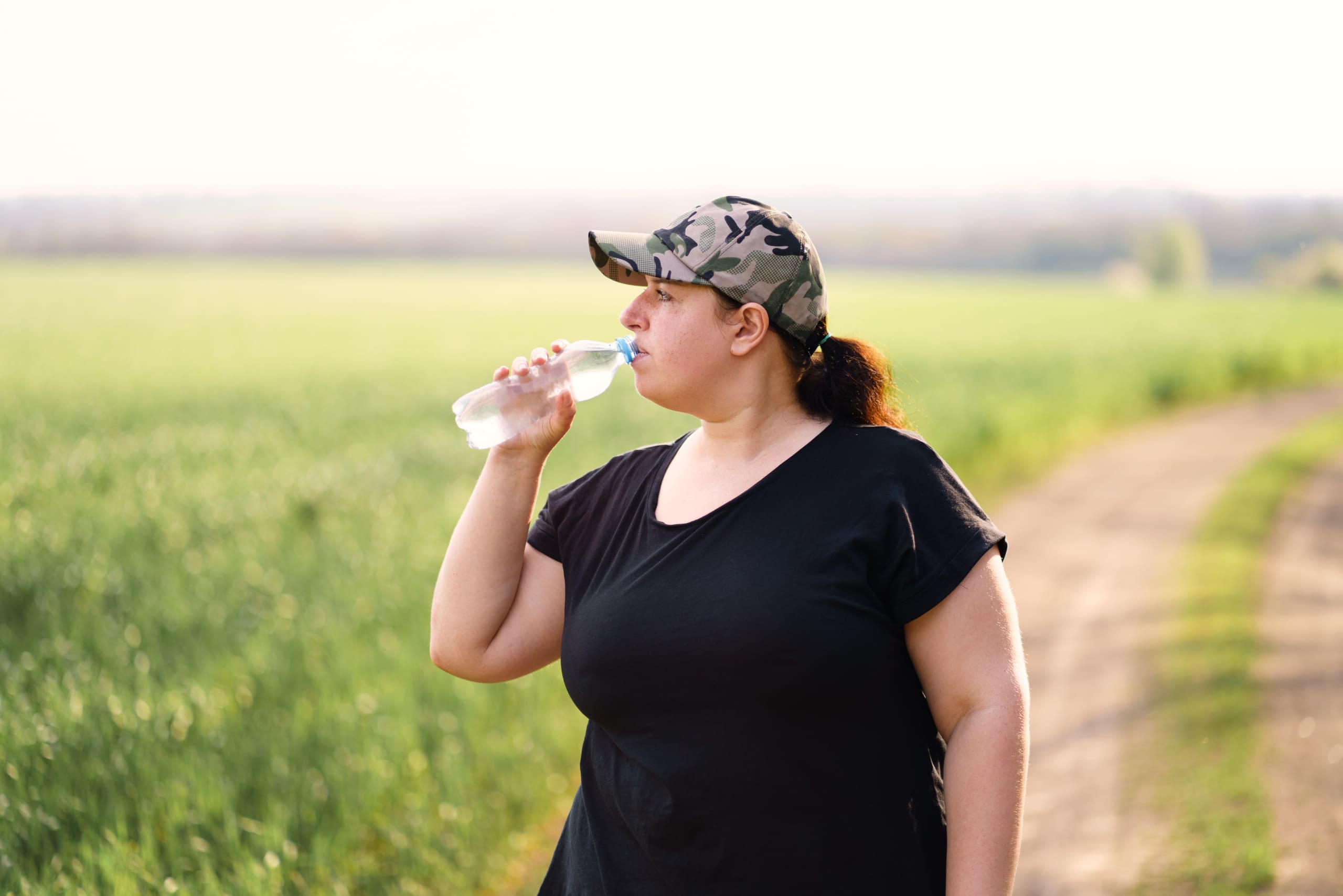 Young woman with metabolic syndrome drinks water after jogging outdoors.