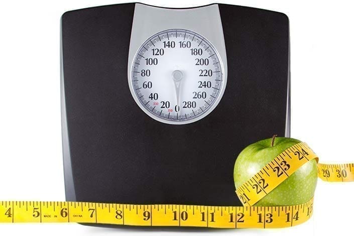 Floor scale with tape measure wrapped around apple to illustrate obesity