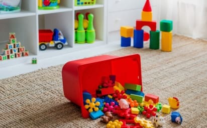 Children's playroom with plastic colorful educational blocks, toys, and games spilling out of a bin onto the floor.