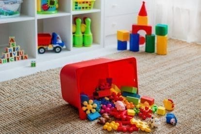 Children's playroom with plastic colorful educational blocks, toys, and games spilling out of a bin onto the floor.
