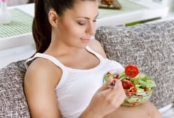 Pregnant woman balancing bowl of salad on belly