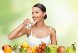 Woman drinking water with fruit sitting in front of her