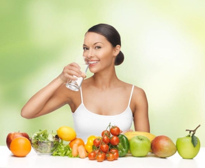 Woman drinking water with fruit sitting in front of her