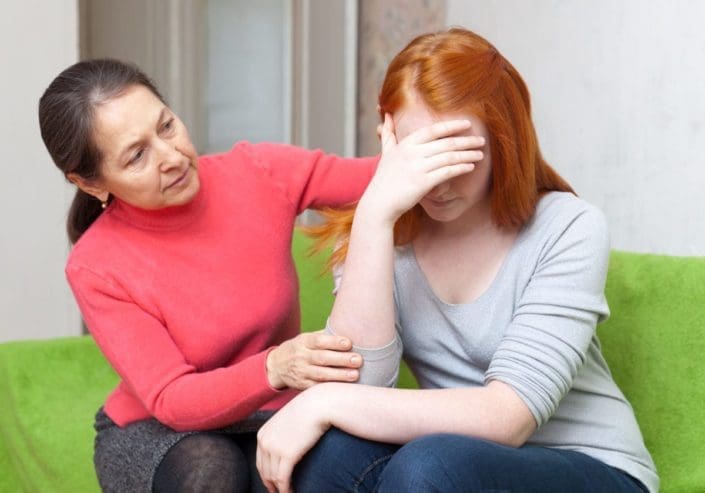 Concerned mother and emotional daughter sitting on couch