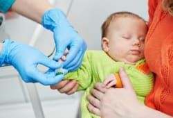 Doctor collecting blood from newborn child in hospital for screening tests
