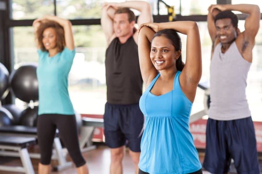 A group of men and women in exercise class doing the same arm stretch