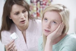 Mother holding condom while talking to teenage daughter about sex