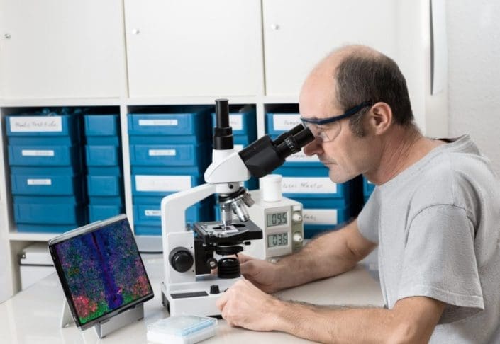 Male scientist or tech observes biopsy sample under a microscope