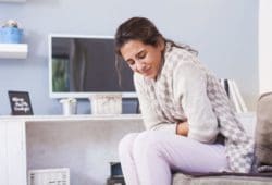 Woman sitting on a couch holding stomach in pain