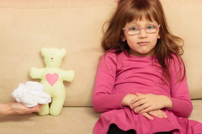 Little girl sitting on sofa next to teddy bear and small shoes for unborn sibling