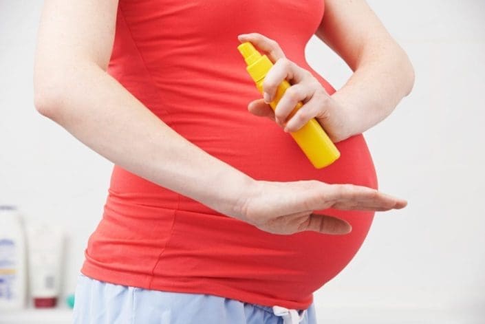 Pregnant woman spraying mosquito repellent on herself