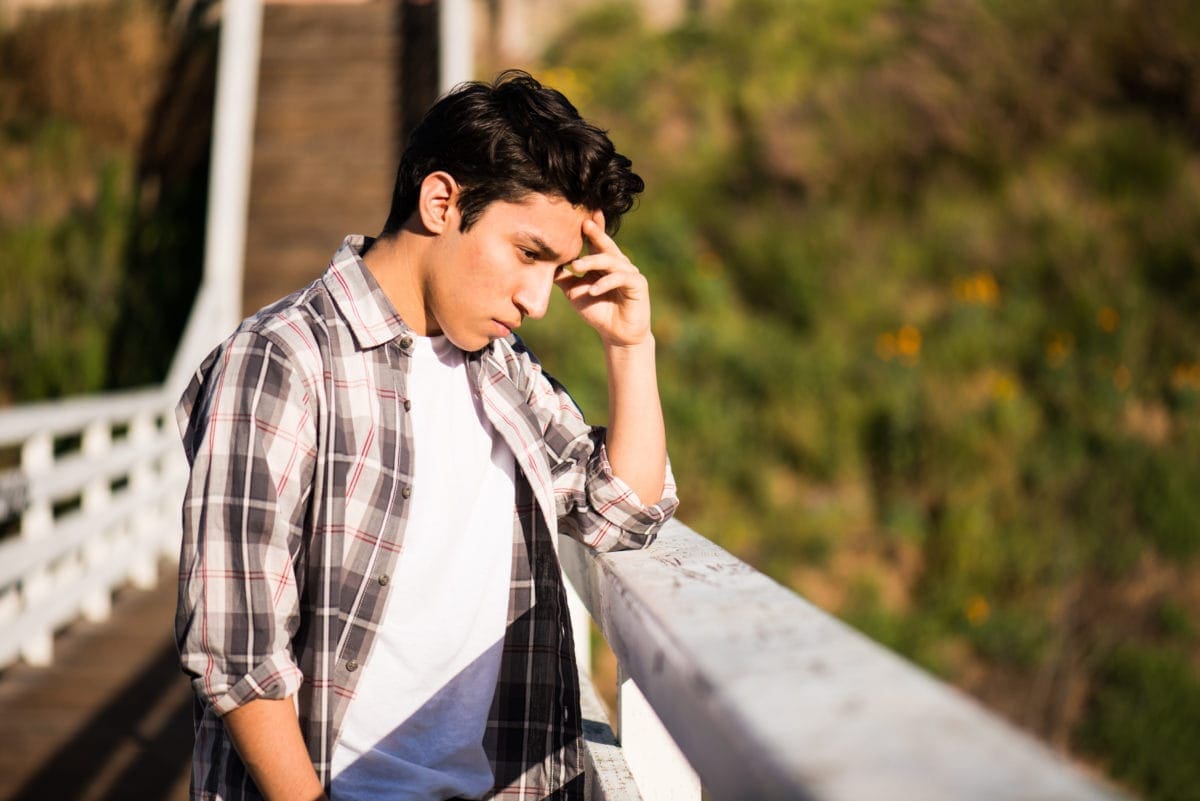 Sad-looking teenage boy standing on a bridge thinking about suicide