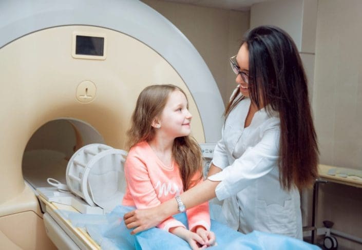 Radiology technician helping position a young girl on the MRI bed