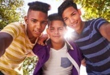Three young teenage boys smiling at camera