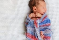 A sleeping baby lays wrapped in a blanket. Phenylketonuria (PKU) is a rare genetic condition where babies are unable to break down an amino acid. This can lead to brain damage.