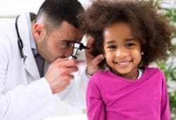 doctor examining the ear of a young smiling girl