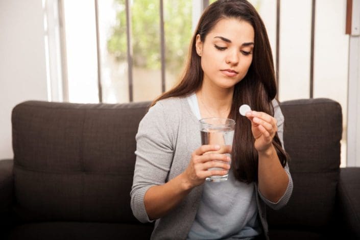 Woman holding antacid tablet and glass of water