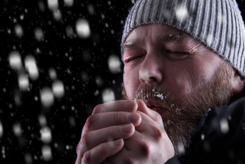 A freezing cold man stands outside in the falling snow at night. Hypothermia occurs when you are exposed to bitter cold for a long time and your body temperature drops below 95°F.