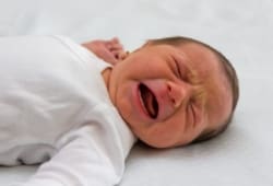 Newborn baby girl crying and laying on bed in hospital