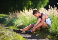Young male runner sitting on the ground holding his sprained ankle in pain