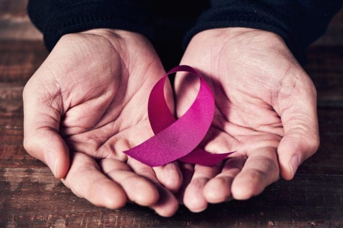 Close-up of a pink ribbon (the symbol of breast cancer awareness) in a man’s hands